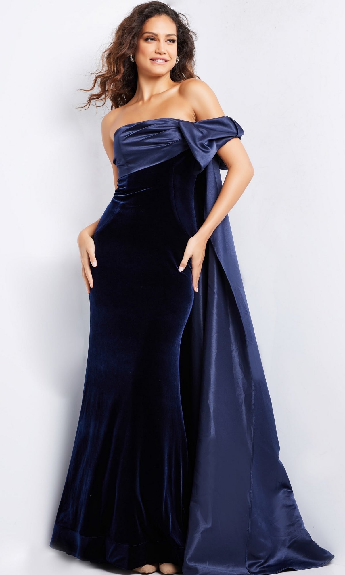 A woman models the Long Prom Dress 37391 by Jovani, a floor-length, navy blue velvet fitted gown with elegant satin draped detail, set against a plain white background.